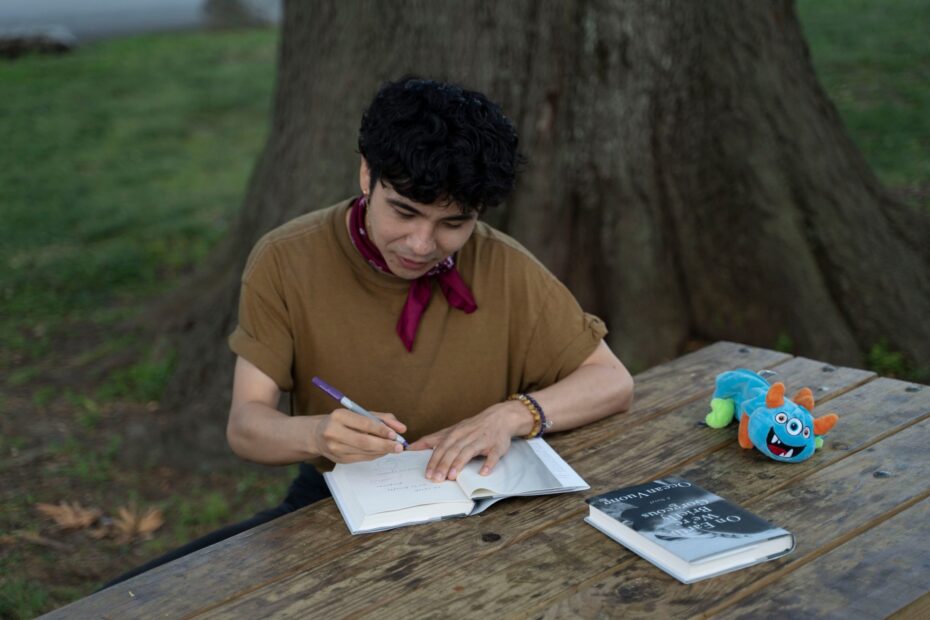 A imagem inclui uma foto colorida do escritor Ocean Vuong, que assina um exemplar do romance objeto da resenha.