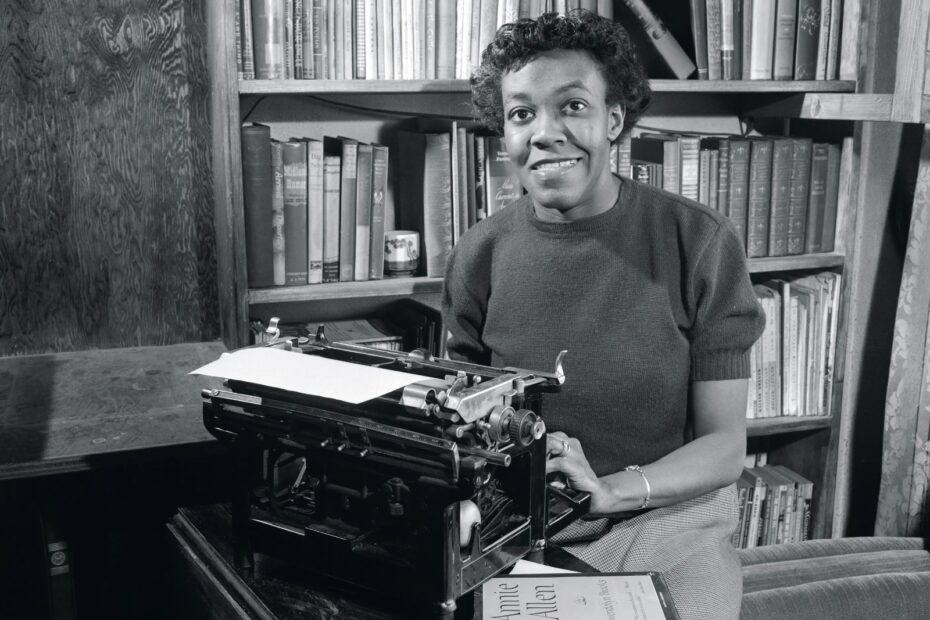 A imagem mostra a autora, Gwendolyn Brooks, com uma máquina de escrever e livros ao fundo, em preto e branco.