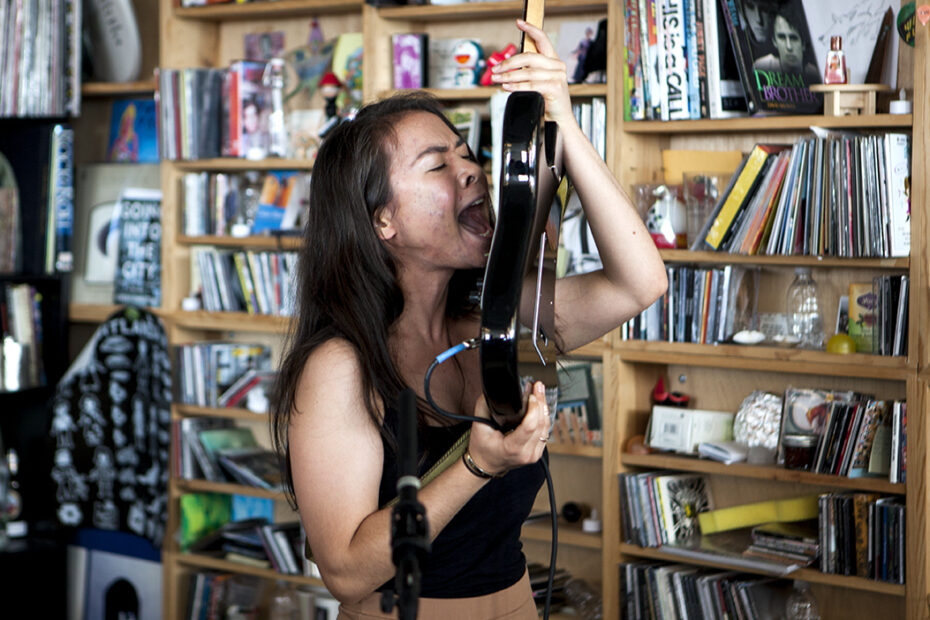 A imagem apresenta a cantora Mitski segurando uma guitarra na altura da cabeça, gritando em direção as cordas em uma performance de "Class of 2013".