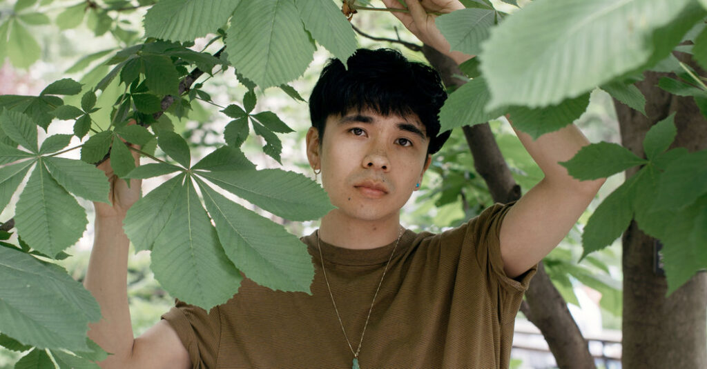 A imagem colorida apresenta o autor ocean Vuong em meio a algumas plantas. A foto é colorida e o homem tem cabelos escuros e utiliza blusa marrom.