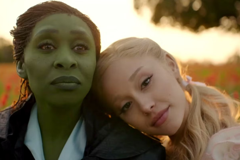 A imagem é um trecho do filme "Wicked", em que Galinda (Ariana Grande) aparece apoiada no ombro de sua amiga, Elphaba (Cynthia Erivo)